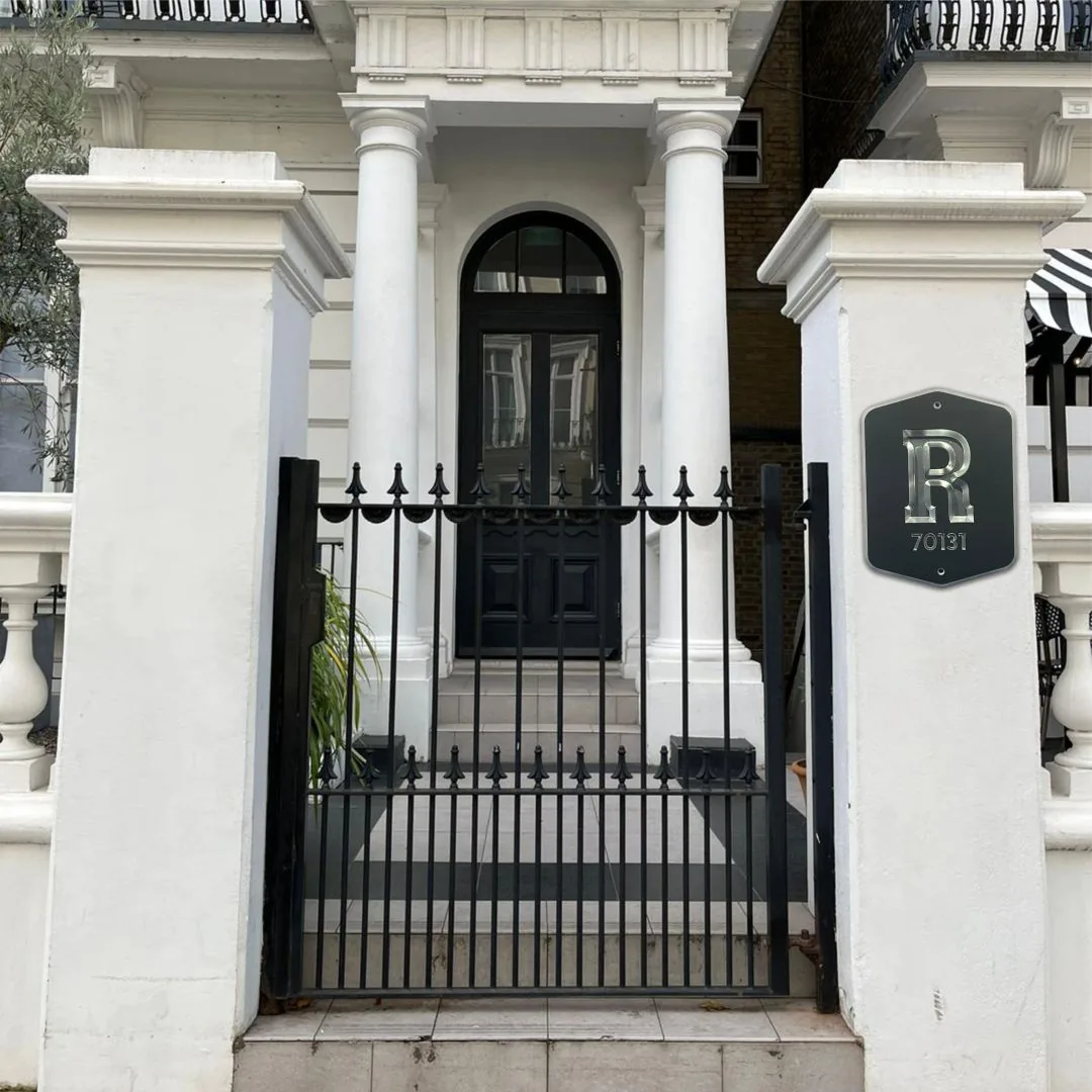 White gate pillars with an iron gate and a black R monogram plaque