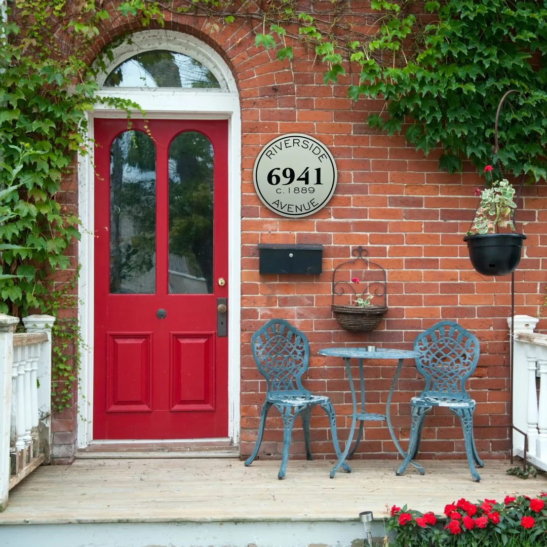 Round historic house sign reading 6941 Riverside Avenue c. 1889 on a brick house beside a red door