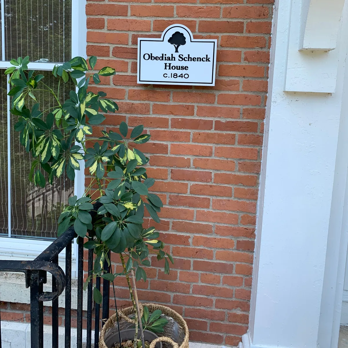 Small historic house name sign on a brick wall beside a white entry