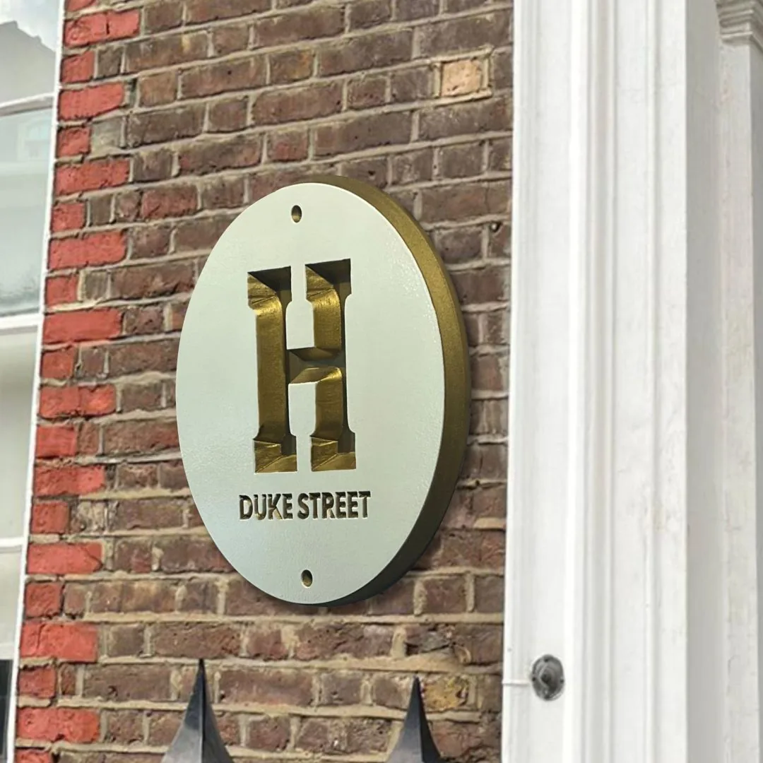 Round cream house plaque with a gold dimensional H and Duke Street on brick