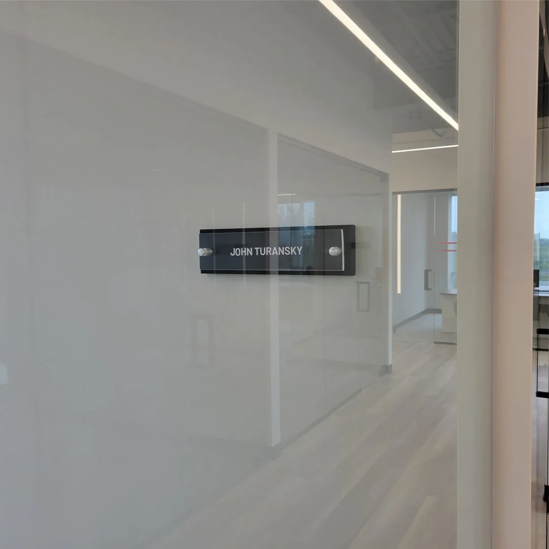Acrylic name sign on a glass office wall along a corridor