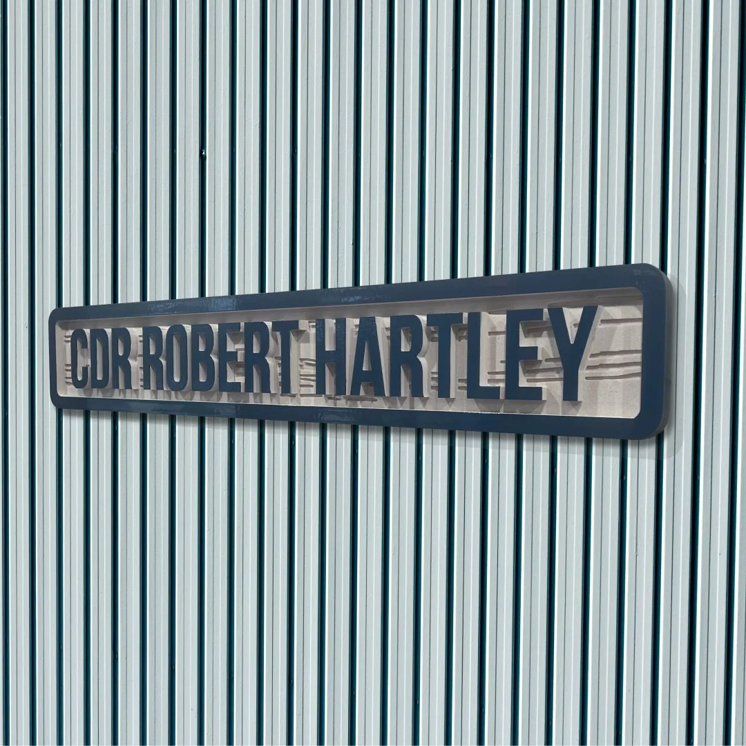 Close view of a routed squadron name sign reading CDR Robert Hartley with raised painted letters