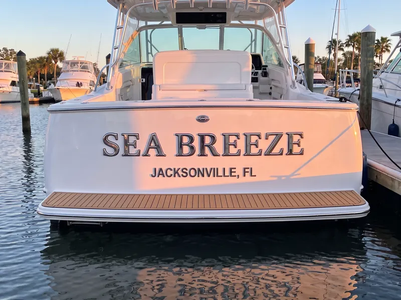 Raised stainless steel boat name and hailing port letters on a white boat transom at a marina